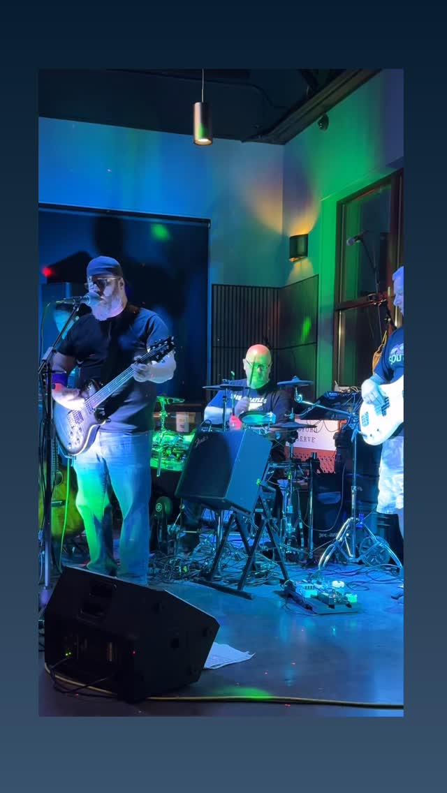 Bass player singing backup with the drummer behind him in green and blue light