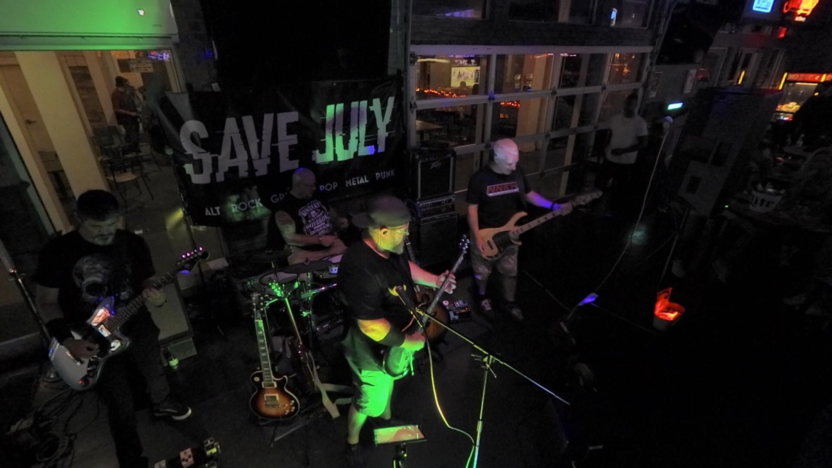 Save July on stage lit green beneath their banner